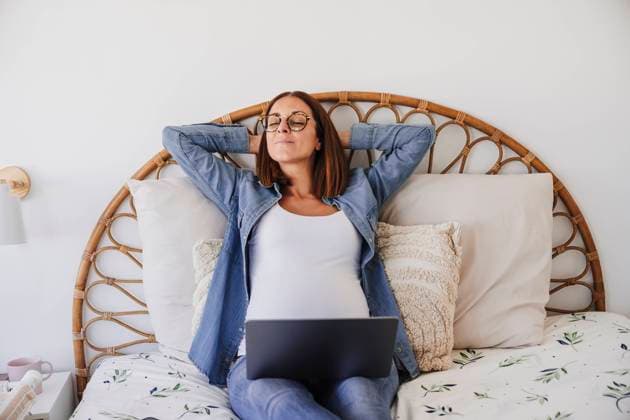 Pregnant freelancer resting on bed with hands behind head at home office model released, Symbolfoto property released, EBBF08707