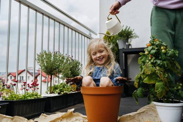 Father watering playful girl sitting in pot at balcony model released, Symbolfoto property released, NSTF00016