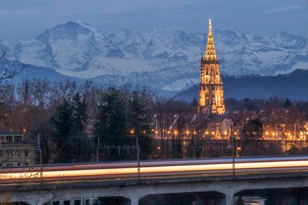 Switzerland, Bern Canton, Bern, Long exposure of passing train at dusk with Bern Minster and Alps in background, KEBF02850