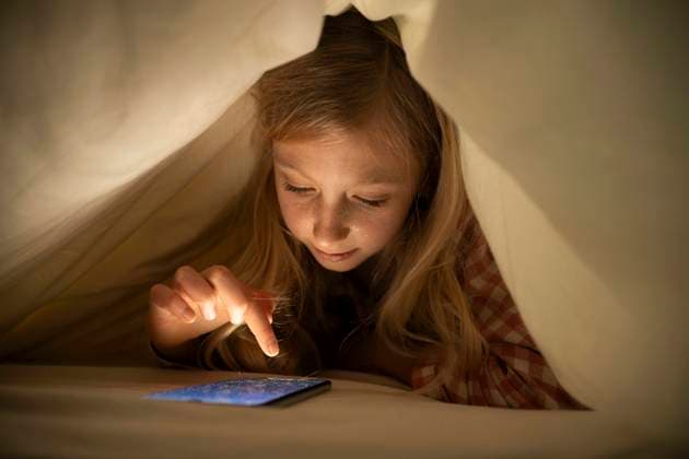 Creative Highlights Symbolbilder Girl using smart phone under blanket on bed at home model released, Symbolfoto property released, NJAF00878