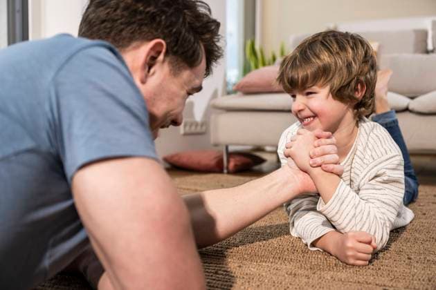 Happy son arm wrestling with father on carpet at home model released, Symbolfoto property released, UUF31390