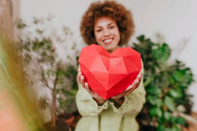 Creative Highlights Symbolbilder Smiling young woman holding red paper heart near plants model released, Symbolfoto property released, YTF01830