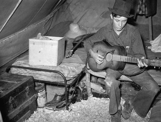 MIGRANT FARMER, 1939. A migrant strawberry picker playing guitar in his tent near Hammond, Louisiana. Photograph by Russell Lee, April 1939.  Copyright: xGRANGERx xGRANGERx 0108393
