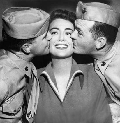 JOAN CRAWFORD (1908-1973). American actress. Crawford receiving kisses from two Marine sergeants as she recovered at home from an appendectomy, 1950.  Copyright: xGRANGERx xGRANGERx 0170127