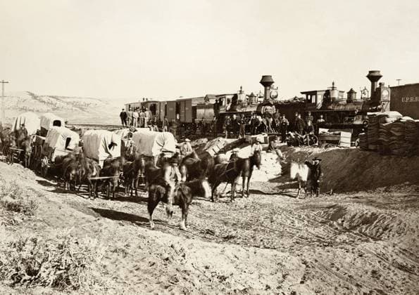 SUPPLY TRAINS,1869. Two locomotive supply trains on the Union Pacific Railroad line with Horsedrawn covered wagons and railroad workers, Wyoming. Photograph by Andrew Joseph Russell, 1869.  Copyright: xGRANGERx xGRANGERx 0652891