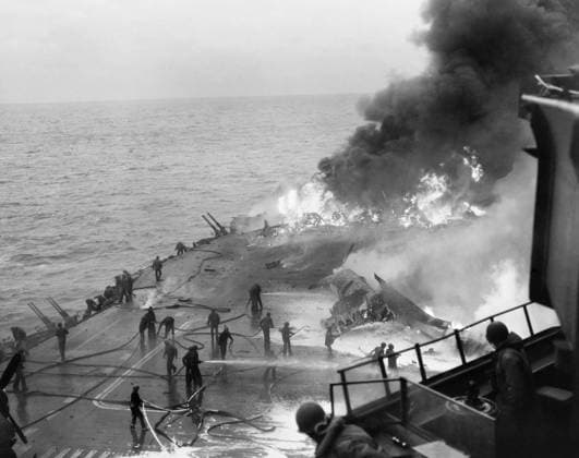 WWII: USS SARATOGA, 1945. Firefighters battle flames on a Vought F4U Corsair fighter plane on the foreword part of the flight deck on the USS Saratoga, after the ship was hit by several Kamikazes off the coast of Iwo Jima, Japan. Photograph, 21 February 1945.  Copyright: xGRANGERx xGRANGERx 0908905