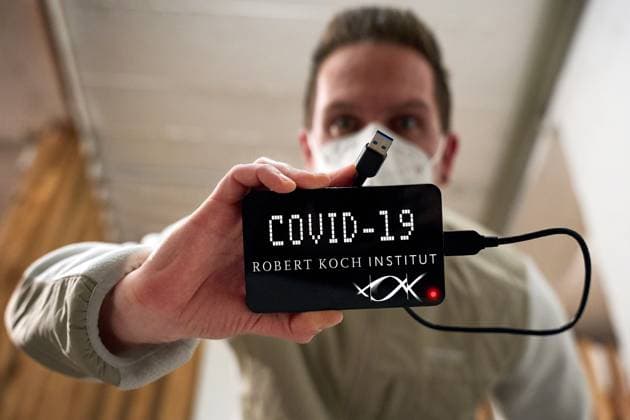 Augsburg, Bavaria, Germany - March 28, 2024: Symbolic photo Robert Koch Institute protocols on Covid-19. A man with FFP-2 mask holds a hard disk with RKI logo and the lettering: Covid-19 in a cellar. PHOTOMONTAGE *** Symbolfoto Robert Koch Institut Protokolle zu Covid-19. Ein Mann mit FFP-2 Maske hält in einem Keller eine Festplatte mit RKI Logo und dem Schriftzug: Covid-19. FOTOMONTAGE