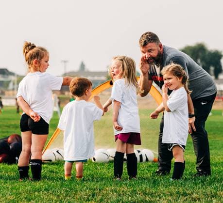 IMAGO Creative, Lifestyle, Frühling in der Stadt Cute kids huddling on soccer field with their coach Missoula, Montana, United States R_VBED240330C-1381091-01 EDITORIAL USE ONLY