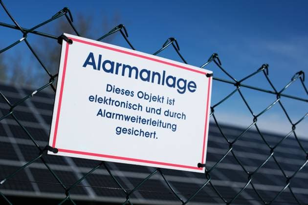Hinweis auf Sicherung durch eine Alarmanlage am Zaun einer Solaranlage.