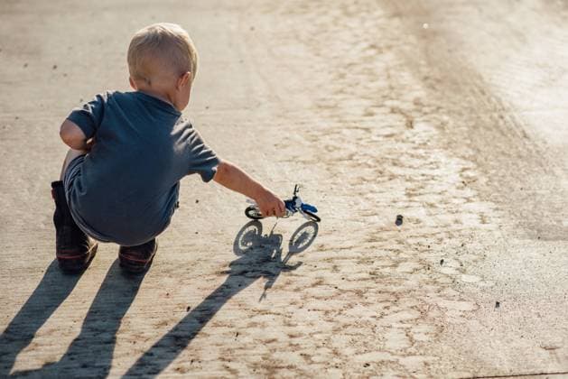 Creative Highlights Symbolbilder Rear view of boy playing with toy motorcycle on driveway in summer United States, North Dakota, Bismarck CR_KIFR240402-1377274-01 ,model released, Symbolfoto