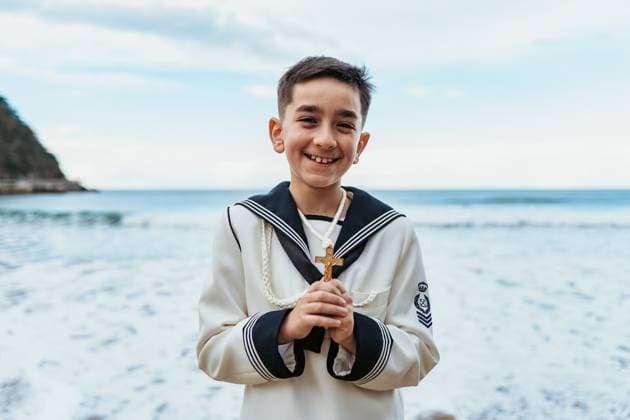 Creative Highlights Symbolbilder A beaming boy holding a crucifix stands by the sea, dressed in his First Communion sailor suit, embodying joy and faith Model Released HodeiUnzueta_ID20559_607218_005 Copyright: xHodeixUnzuetax