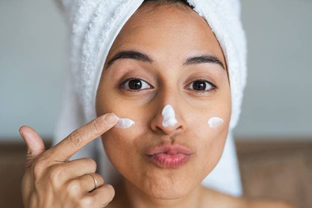 Creative Highlights Symbolbilder Woman in a towel wrap applying facial cream to her cheeks with a playful expression Model Released PabloMenendez_ID20332_601463_052 Copyright: xPabloxMenendezx