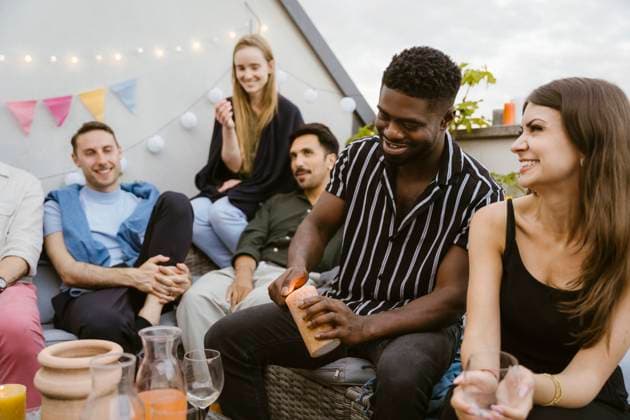 Smiling young man burning candle while sitting with male and female friends at party Germany, Berlin, model released, property released Copyright: xMaskotx , MA108190 MA108190