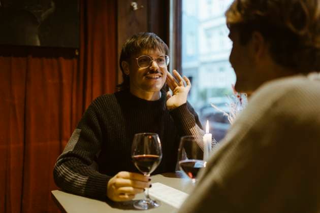 Smiling gay man holding wineglass and talking with boyfriend while sitting at restaurant Germany, Berlin, model released, property released Copyright: xMaskotx , MA108444 MA108444
