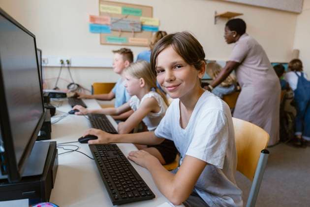 Portrait of smiling male pupil sitting with friends at desk in computer classroom Germany, Berlin, model released, property released Copyright: xMaskotx , MA108584 MA108584