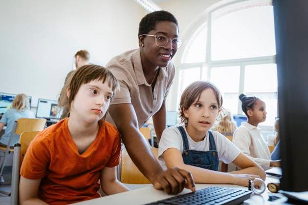 Smiling female teacher assisting girl with down syndrome in computer class at school Germany, Berlin, model released, property released Copyright: xMaskotx , MA108598 MA108598