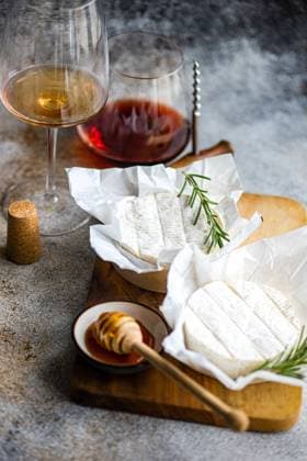 An exquisite display of Brie cheese complemented by honey, rosemary, and a pairing of red and white wine. Model Released AnnaBogush_ID20594_608288_007 Copyright: xAnnaxBogushx