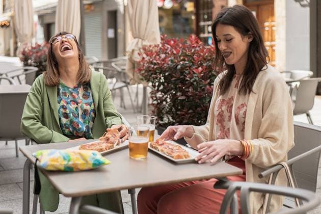 IMAGO Creative, Lifestyle, Frühling in der Stadt Two joyful women sharing a moment of laughter while eating pizza and having drinks at an outdoor cafe, highlighted by springtime attire Model Released HodeiUnzueta_ID20733_612062_023 Copyright: xHodeixUnzuetax