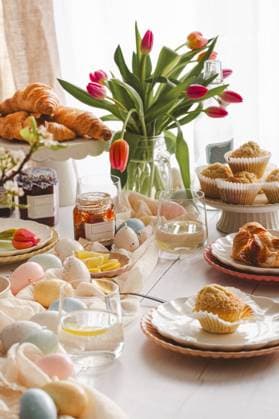 An inviting Easter breakfast table featuring fresh croissants, coconut muffins, marmalade jars, and a bouquet of tulips among colorful eggs and tableware, reflecting spring vibes and family time Model Released JoannaFufal_ID20588_608222_002 Copyright: xJoannaxFufalx