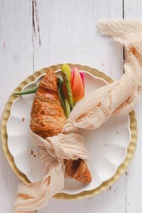 An Easter-themed croissant wrapped with a rustic cloth, adorned with a vibrant tulip, presented on a decorative plate, invoking the essence of spring Model Released JoannaFufal_ID20588_608223_003 Copyright: xJoannaxFufalx