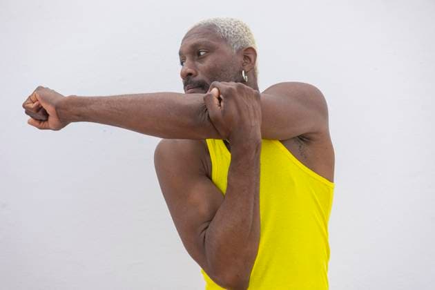 Creative Highlights Symbolbilder An athlete in a vibrant yellow tank stretches his arm muscles, preparing for a street basketball game with determination on his face Model Released JuanAizpuru_ID20351_602322_003 Copyright: xJuanxAizpurux