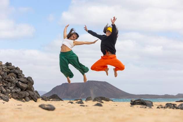 A joyful same-sex couple leaps into the air on a sandy beach, with a scenic mountain backdrop, embodying freedom and happiness Model Released JuanAizpuru_ID20478_604918_019 Copyright: xJuanxAizpurux