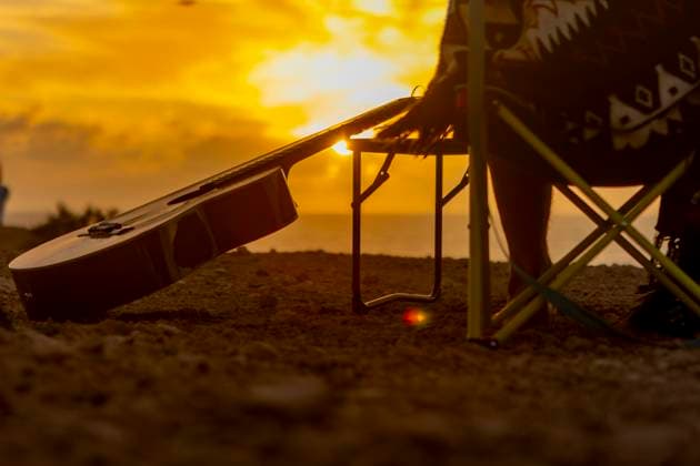Back view of crop unrecognizable nomadic musician s guitar resting at a beachside campsite during a golden sunset, symbolizing inspiration and wanderlust. Model Released JuanAizpuru_ID20562_607331_033 Copyright: xJuanxAizpurux