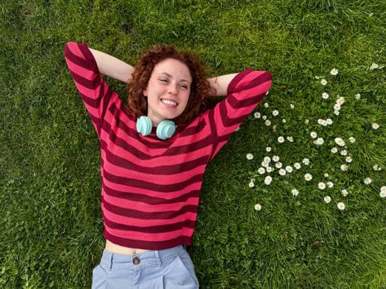 IMAGO Creative: Sommer, Sommertage im Stadtpark A happy young redhead woman with curly red hair lies on a lush green lawn, surrounded by white daisies, enjoying a leisurely day Model Released ManuelRuiz_ID20916_617113_046 Copyright: xManuelxRuizx
