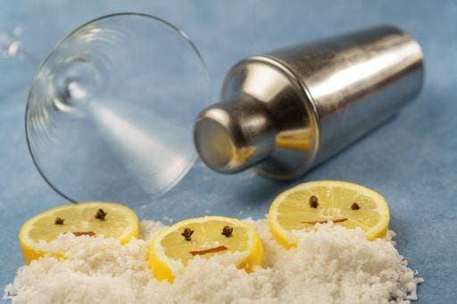 lemon slices with cloves and cinnamon forming a smiley face on a pile of salt next to a cocktail shaker and a crystal glass with blue background 23592764 RECORD DATE NOT STATED