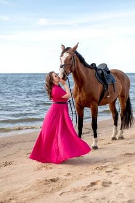 Creative Highlights Symbolbilder A woman in a pink dress standing next to a horse on the sandy beach 23637424 ,model released, Symbolfoto RECORD DATE NOT STATED