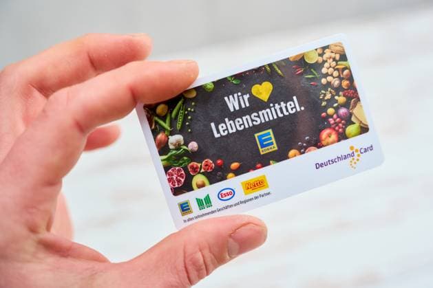 Augsburg, Bavaria, Germany - April 17, 2024: A customer s hand holds a Deutschland Card. Bonus program customer card from Edeka, Netto, Esso and Marktkauf *** Hand von einem Kunden hält eine Deutschland Card. Bonusprogramm Kundenkarte von Edeka, Netto, Esso und Marktkauf