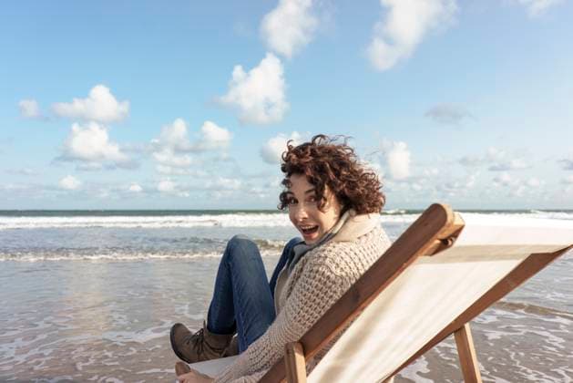 Creative Highlights Symbolbilder Cheerful woman sitting on deck chair looking back at beach model released, Symbolfoto, KNSF10196