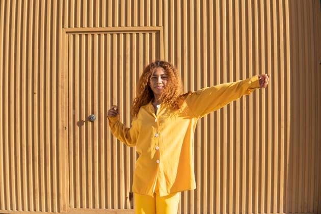 Woman with curly hair wearing yellow casuals standing in front of metal wall on sunny day model released, Symbolfoto, MGRF01152