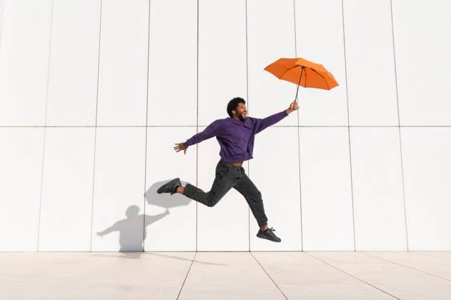Creative Highlights Symbolbilder Cheerful man jumping with orange umbrella in front of white wall model released, Symbolfoto, VRAF00476