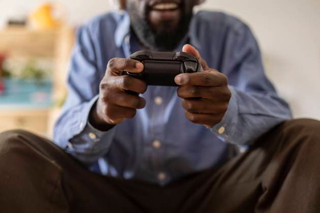 Non-binary person holding controller and playing video game at home model released, Symbolfoto property released, JCCMF11569