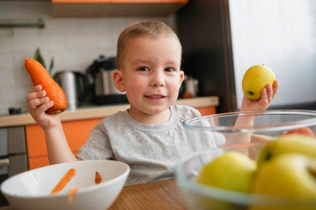 Creative Highlights Symbolbilder Smiling boy holding apple and carrot in kitchen at home model released, Symbolfoto property released, KVBF00096