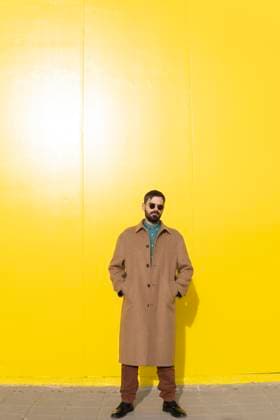 Creative Highlights Symbolbilder Man wearing long brown coat and standing with hands in pockets near yellow wall model released, Symbolfoto, MGRF01297