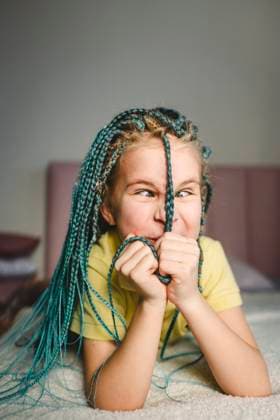 Creative Highlights Symbolbilder Girl playing with turquoise dyed braided hair lying on bed at home model released, Symbolfoto property released, OLRF00256