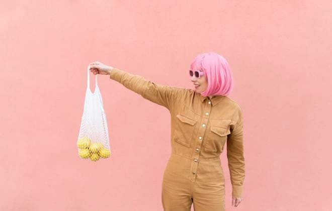 Smiling woman holding mesh bag with lemons in front of pink wall model released, Symbolfoto, VRAF00503