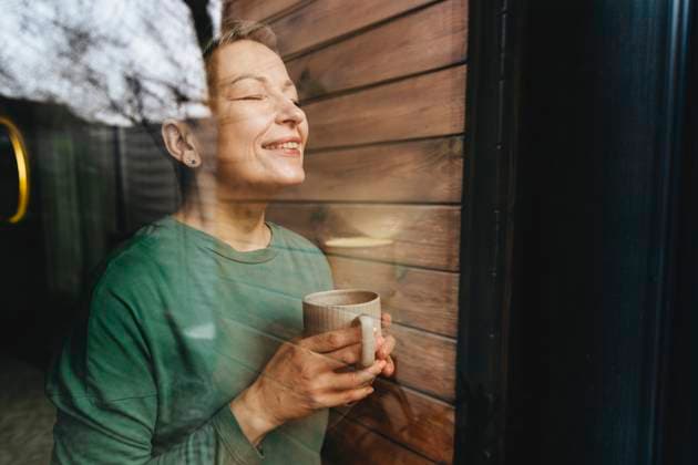 Creative Highlights Symbolbilder Smiling woman with eyes closed holding coffee mug behind glass window model released, Symbolfoto property released, YTF02122