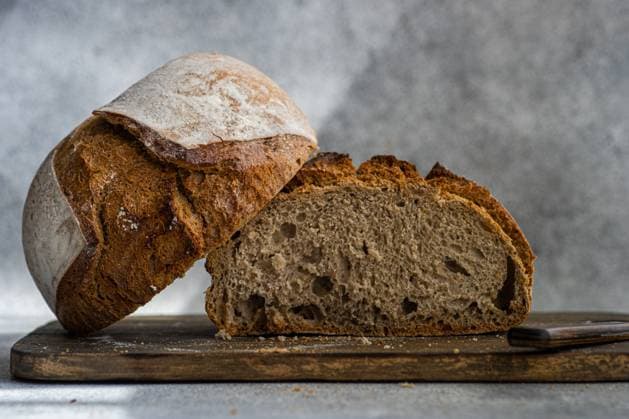 A loaf of homemade rye sourdough bread, sliced open to reveal its airy texture, sits on a rustic wooden cutting board with a knife beside it Model Released AnnaBogush_ID21101_622341_006 Copyright: xAnnaxBogushx