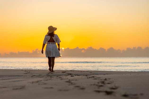 Back view of an unrecognizable woman enjoying a peaceful walk along the shore at sunrise, with the warm glow of the sun casting a tranquil backdrop. Model Released JuanAizpuru_ID20865_615527_019 Copyright: xJuanxAizpurux