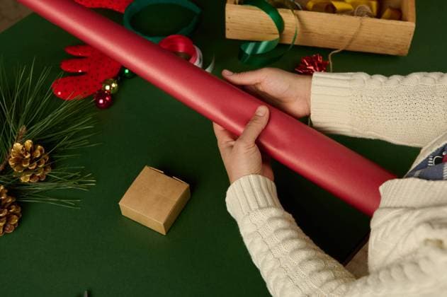 Close-up Woman holds wraping gift paper of red color while packing Christmas or New Year s presents at green background. Top view woman s hands hold gift wrapping paper of red color while packing Christmas or New Year s presents, on green background. Festive decorations in wooden crate.Boxing Day. Xmas. December 25th Copyright: xTarasxGrebinets RECORD DATE NOT STATED