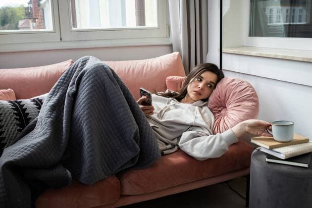 Young woman lying on coach with the phone and drinking tea Sopot, Pomeranian Voivodeship, Poland R_QAGC24050147-1419042-01 ,model released, Symbolfoto