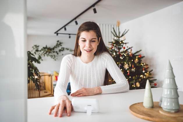 Smiling young woman watching the baby monitor from the kitchen Young caucasian woman dressed in white sitting by the white kitchen island looking at the baby monitor, watching her baby sleep. Copyright: x RECORD DATE NOT STATED