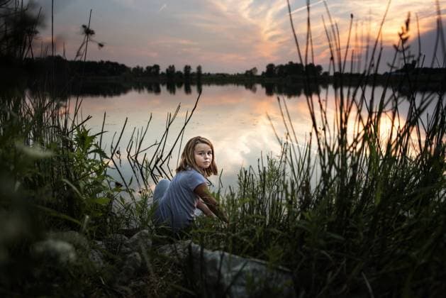 Creative Highlights Symbolbilder Beautiful. young girl peeking through tall grass on lake at sunset Wooster, Ohio, United States CR_JOKU240507CB-1422587-01 ,model released, Symbolfoto