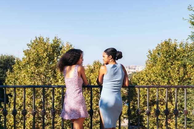 IMAGO Creative: Sommer, Sommertage im Stadtpark Back view of two African-American girls in dresses, looking at the city views and a large urban park while leaning on a bridge railing. They talk and enjoy the day together. Model Released PedroMerino_ID19012_565710_023 Copyright: xPEDROxMERINOx