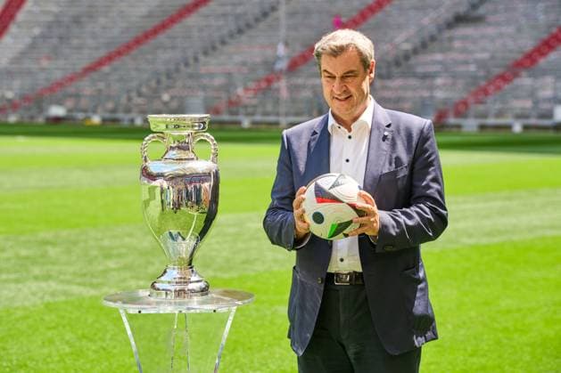 Ministerpräsident Dr. Markus Söder (CSU) auf dem Fußball Spielfeld der Allianz Arena in München. Er steht neben dem Henri-Delaunay-Pokal der UEFA EURO 2024 und hält einen originalen Adidas Fußball der Fußballeuropameisterschaft