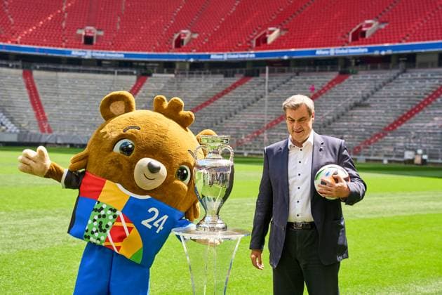Ministerpräsident Dr. Markus Söder (CSU) auf dem Fußball Spielfeld der Allianz Arena in München. Er steht neben dem Henri-Delaunay-Pokal der UEFA EURO 2024 und hält einen originalen Adidas Fußball der Fußballeuropameisterschaft