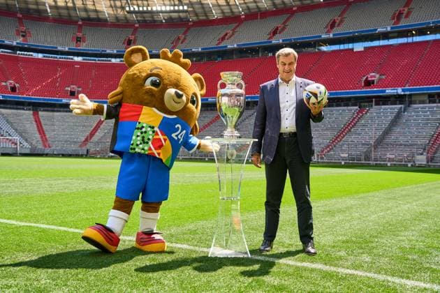 Ministerpräsident Dr. Markus Söder (CSU) auf dem Fußball Spielfeld der Allianz Arena in München. Er steht neben dem Henri-Delaunay-Pokal der UEFA EURO 2024 und hält einen originalen Adidas Fußball der Fußballeuropameisterschaft